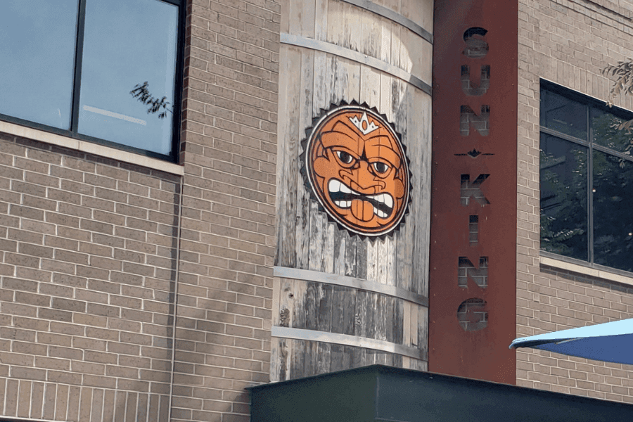 A wooden sign featuring an angry cartoon face and the words "SUN KING" on a brick building.