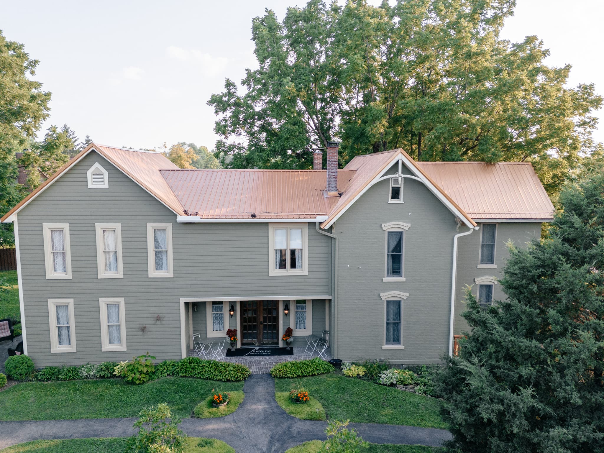 A two-story gray house with a copper roof surrounded by greenery.
