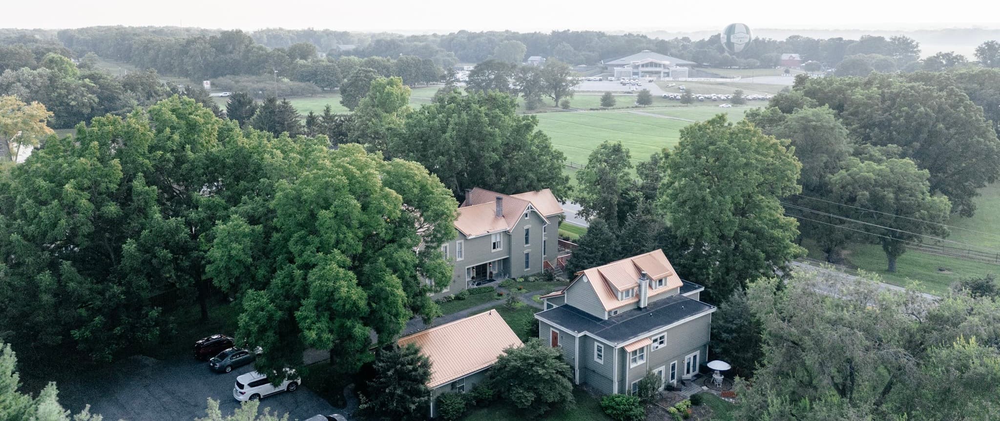 Aerial view of a cluster of houses surrounded by lush greenery and open fields.