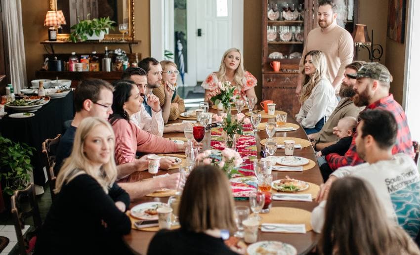 A diverse group of people gather around a long dining table, enjoying a meal and conversation in a cozy indoor setting. A diverse group of people gather around a long dining table, enjoying a meal and conversation in a cozy indoor setting.