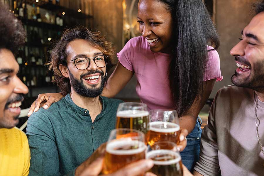 A group of four friends joyfully toasting with drinks in a lively setting.