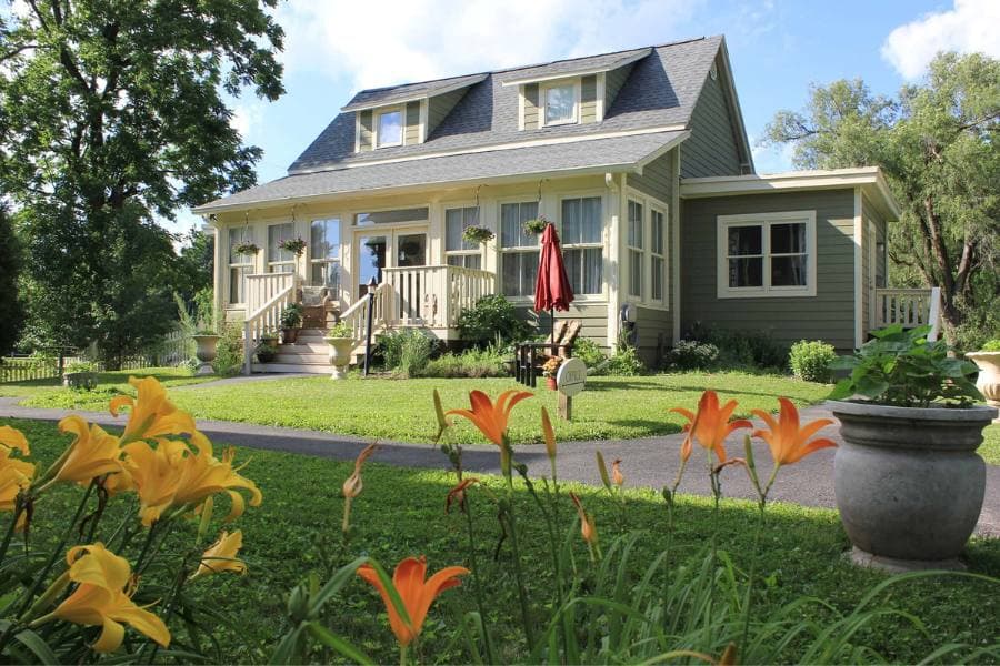 A charming gray house with a porch, surrounded by lush green grass and vibrant orange flowers.