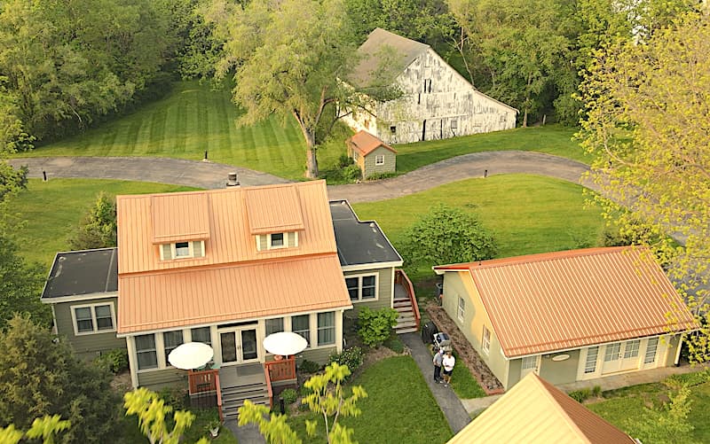 Aerial view of a landscaped property featuring multiple buildings with metal roofs and a gravel path.