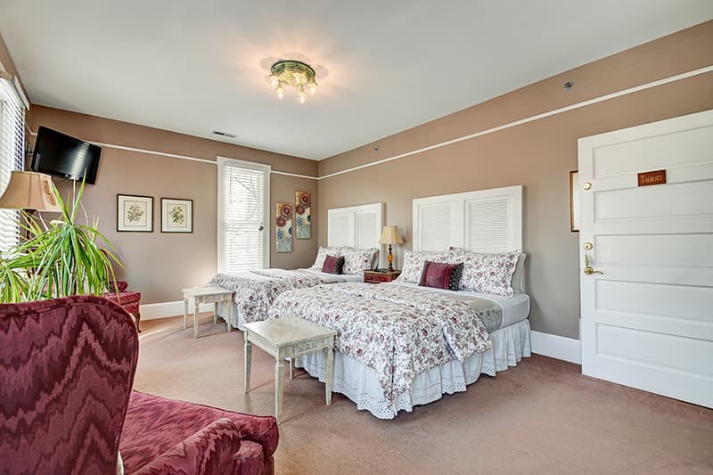 A well-decorated guest room featuring two twin beds, a plush armchair, and natural light from a window.