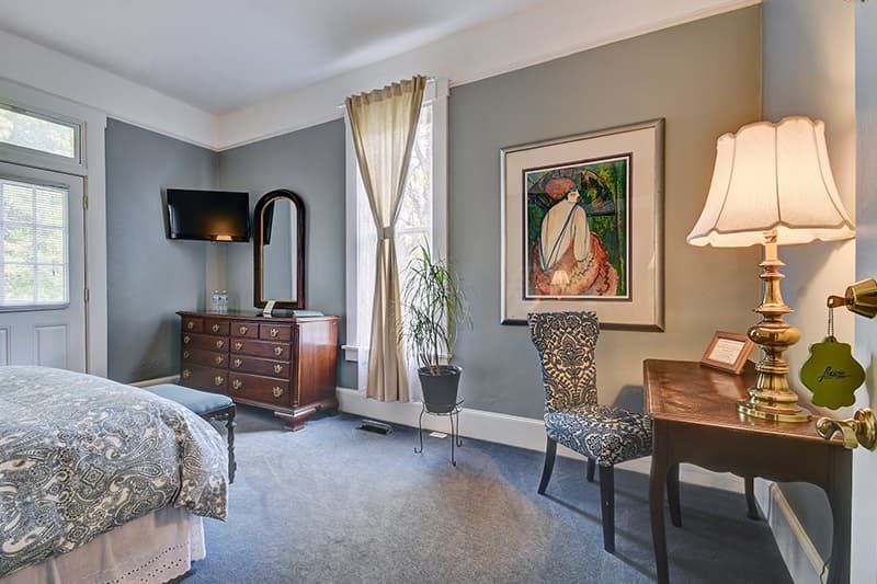 Cozy bedroom featuring a bed, dresser, desk, framed artwork, and natural light from windows.