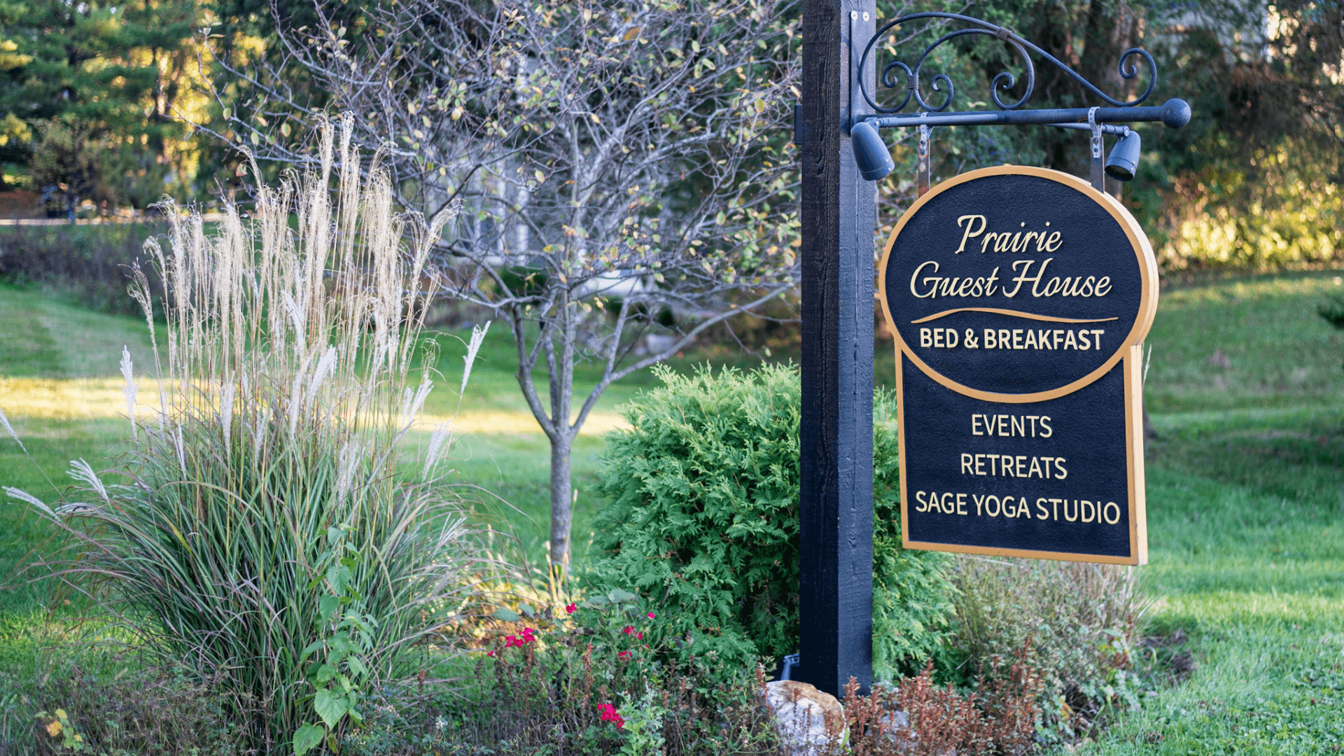 Sign for Prairie Guest House Bed & Breakfast, featuring offerings such as events, retreats, and a yoga studio, amidst a lush green backdrop.