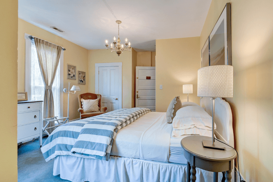 Cozy bedroom with a yellow color scheme, featuring a striped blanket, a chandelier, and a comfortable armchair.