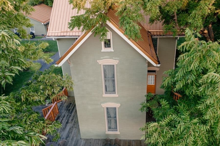 Aerial view of a green house with a metal roof, surrounded by trees.