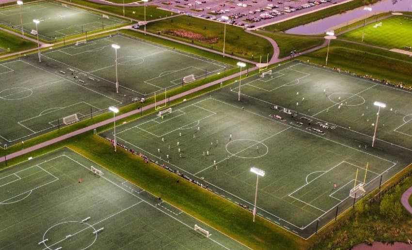 Aerial view of brightly lit soccer fields with players in action and parking in the background. Aerial view of brightly lit soccer fields with players in action and parking in the background.