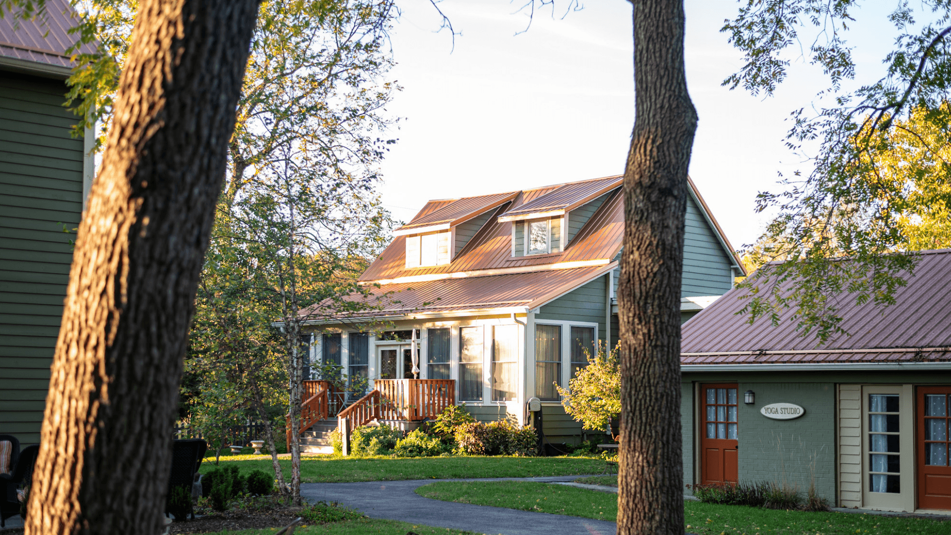 A two-story house with a red metal roof surrounded by greenery and trees.