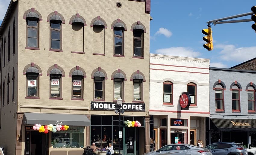 A storefront featuring "NOBLE COFFEE" with colorful balloons outside, flanked by other businesses on a sunny day. A storefront featuring "NOBLE COFFEE" with colorful balloons outside, flanked by other businesses on a sunny day.