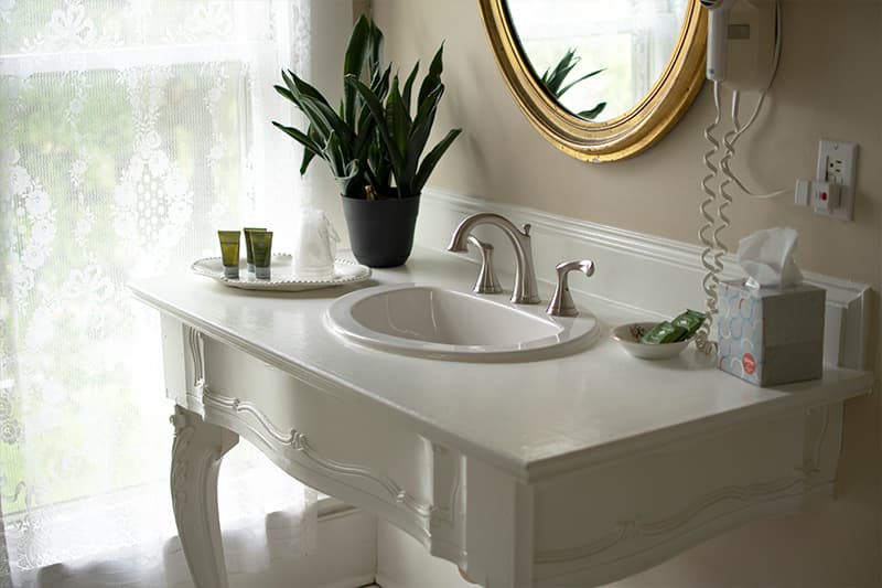 A stylish bathroom vanity with a round mirror, sink, potted plant, and toiletries.