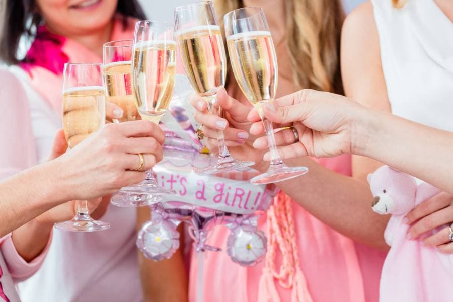 A group of people toast with champagne glasses while celebrating a baby girl with decorations.