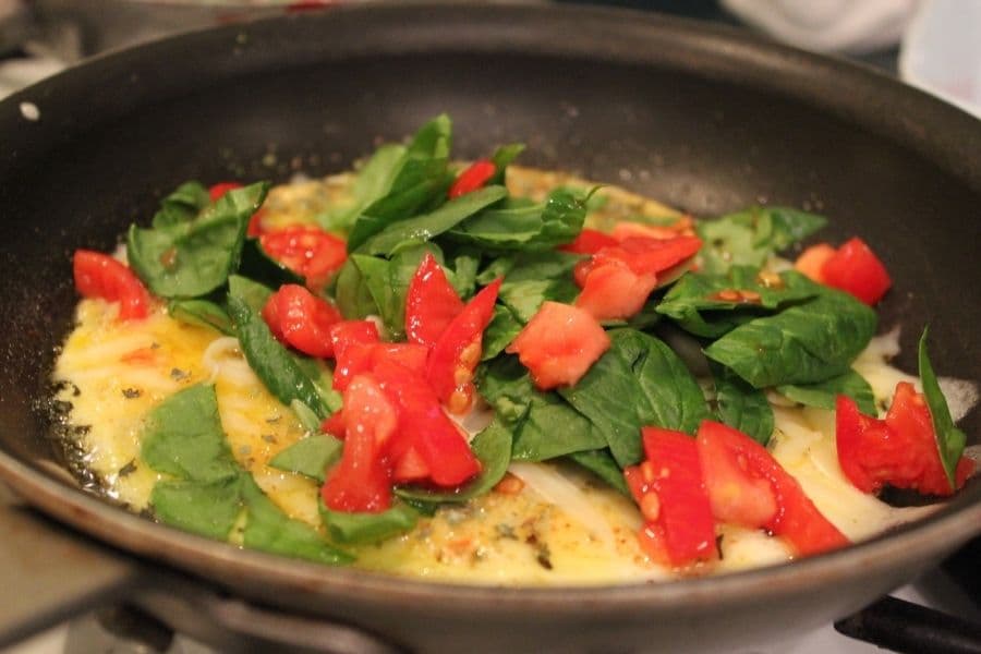 A pan cooking a mixture of spinach, diced tomatoes, and eggs.