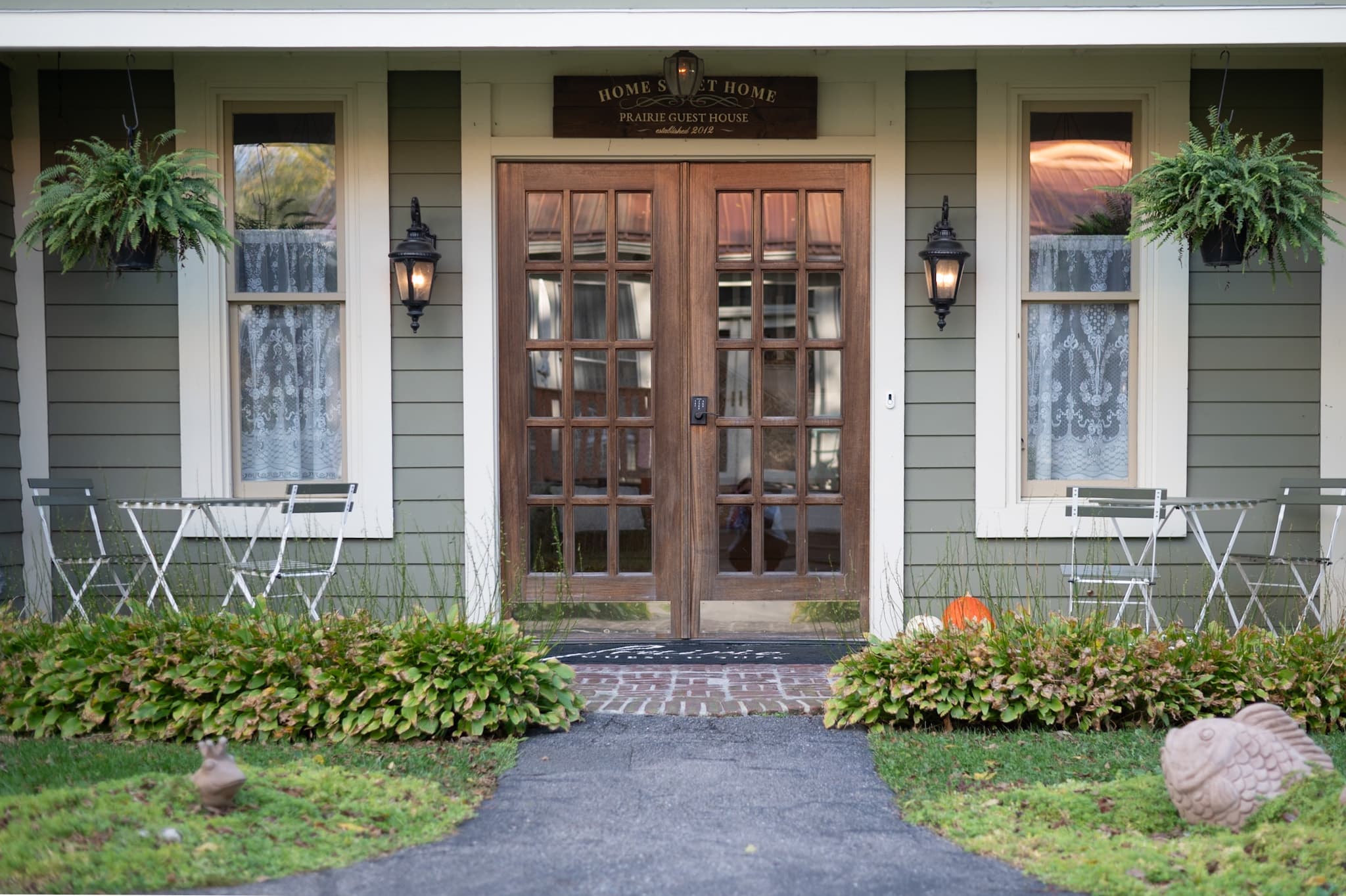 Front entrance of a charming house with wooden doors, outdoor seating, and greenery.