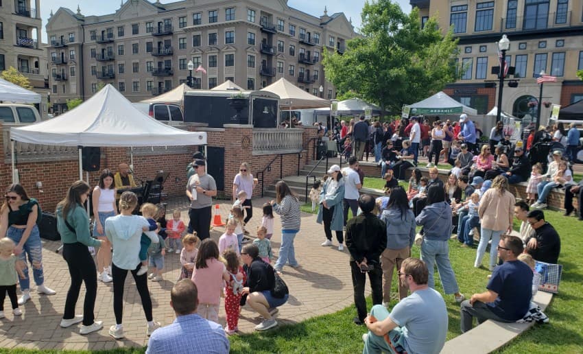 A lively outdoor event with families and children gathered around food stalls and entertainment in a park. A lively outdoor event with families and children gathered around food stalls and entertainment in a park.