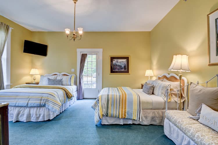 A cozy guest room with two beds, a seating area, and a door leading to an outside patio.
