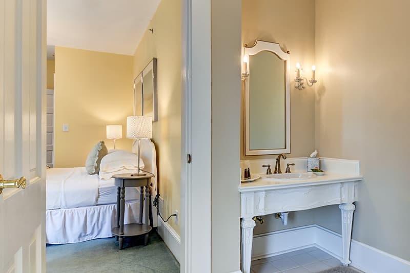 A cozy bedroom with a nightstand and a bathroom featuring a vintage sink and mirror.