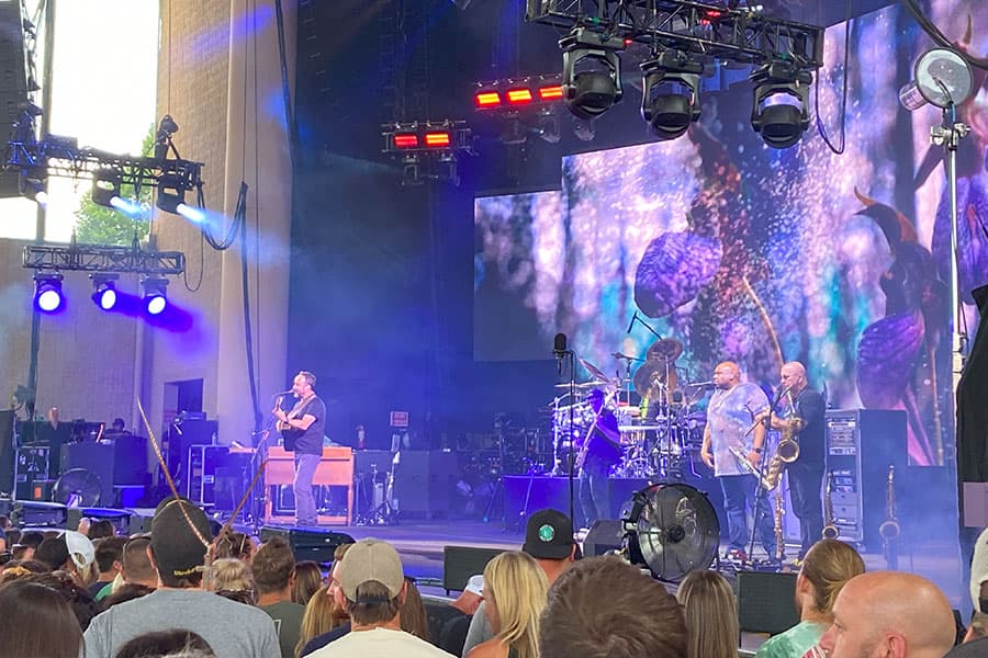 A band performs on stage with vibrant lighting while an enthusiastic audience watches from below.