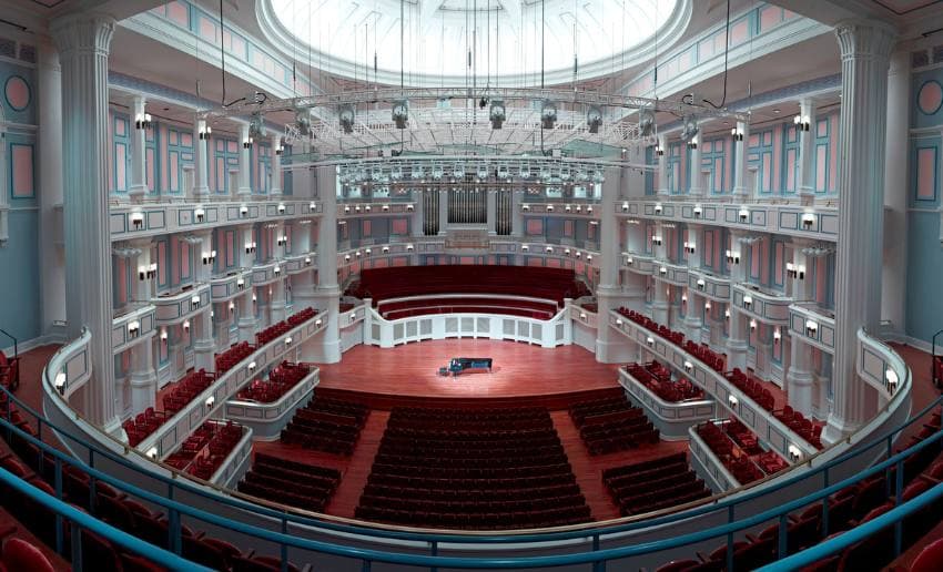 A grand concert hall featuring plush red seating and a grand piano on stage, illuminated by natural light from a skylight. A grand concert hall featuring plush red seating and a grand piano on stage, illuminated by natural light from a skylight.
