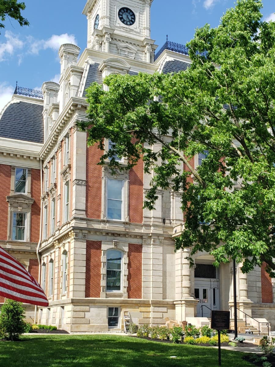 Historic brick building with a clock tower, surrounded by greenery and an American flag in the foreground.