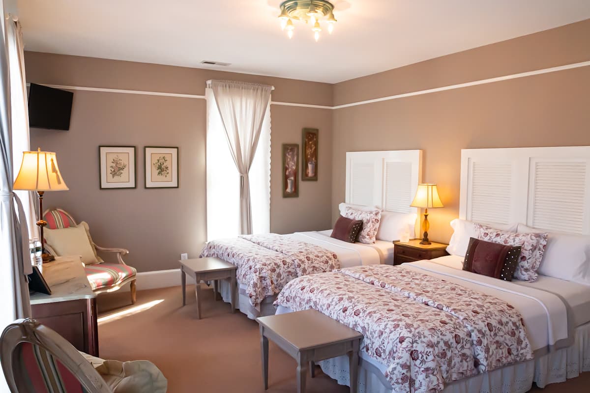 A cozy guest room featuring two twin beds with floral bedspreads and soft lighting, accented by a seating area.