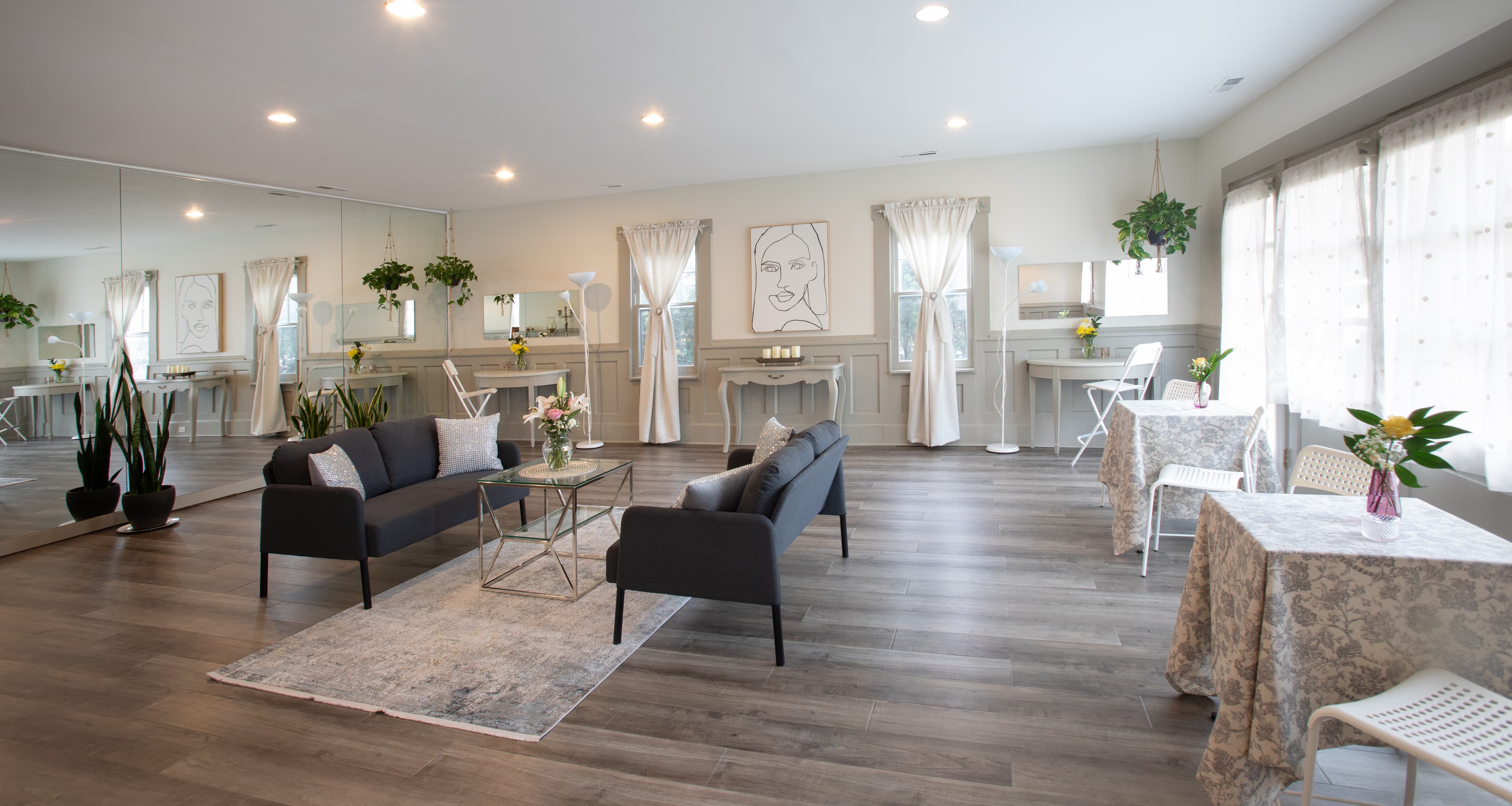 A bright, stylish interior featuring a seating area with plants, a coffee table, and two small tables, all against a mirrored wall.
