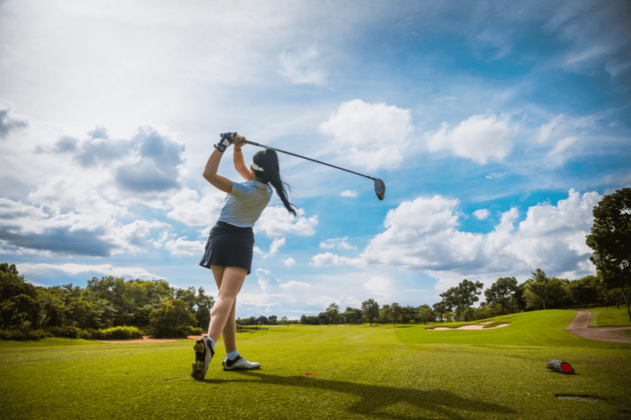 A golfer follows through on a swing under a bright, cloudy sky.