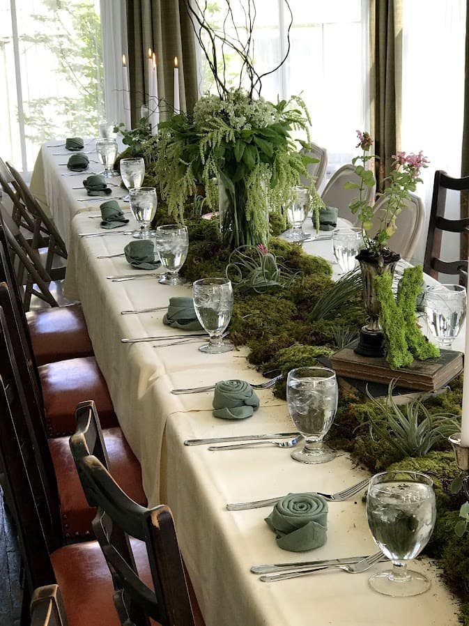 A beautifully set long dining table with moss, floral arrangements, and elegantly folded napkins.