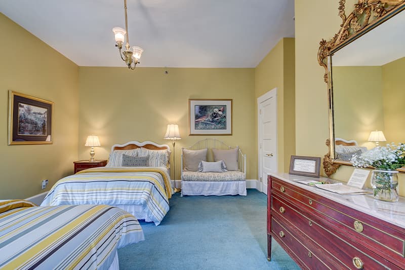 Brightly lit bedroom with two beds, a seating area, and warm yellow walls.