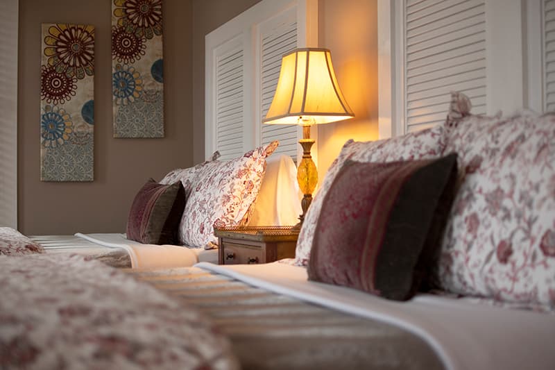 Cozy bedroom with two floral-patterned beds, a bedside lamp, and colorful wall art.