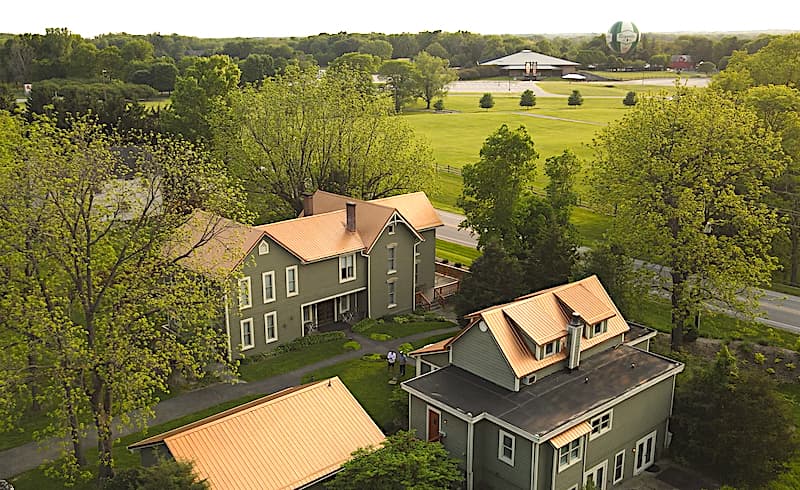 Aerial view of a green house with copper roofs surrounded by trees and an open field.