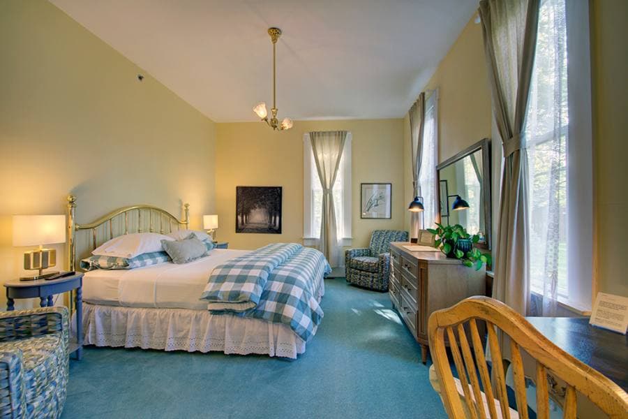 A cozy bedroom featuring a large bed, chairs, and natural light from tall windows.