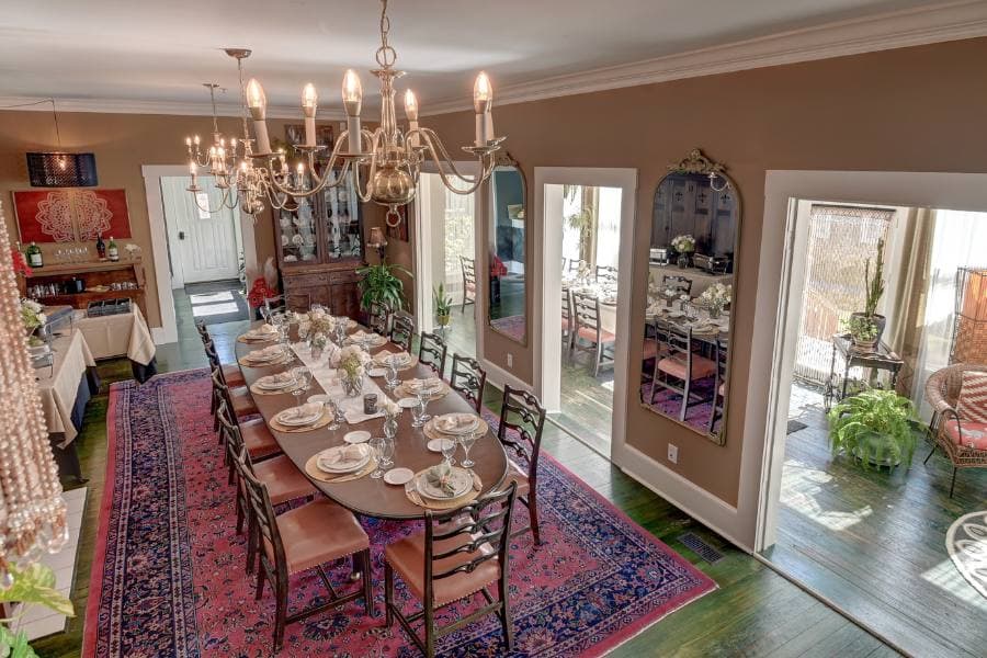 A beautifully set dining table with elegant tableware under a chandelier, framed by mirrors and doors leading to a garden.