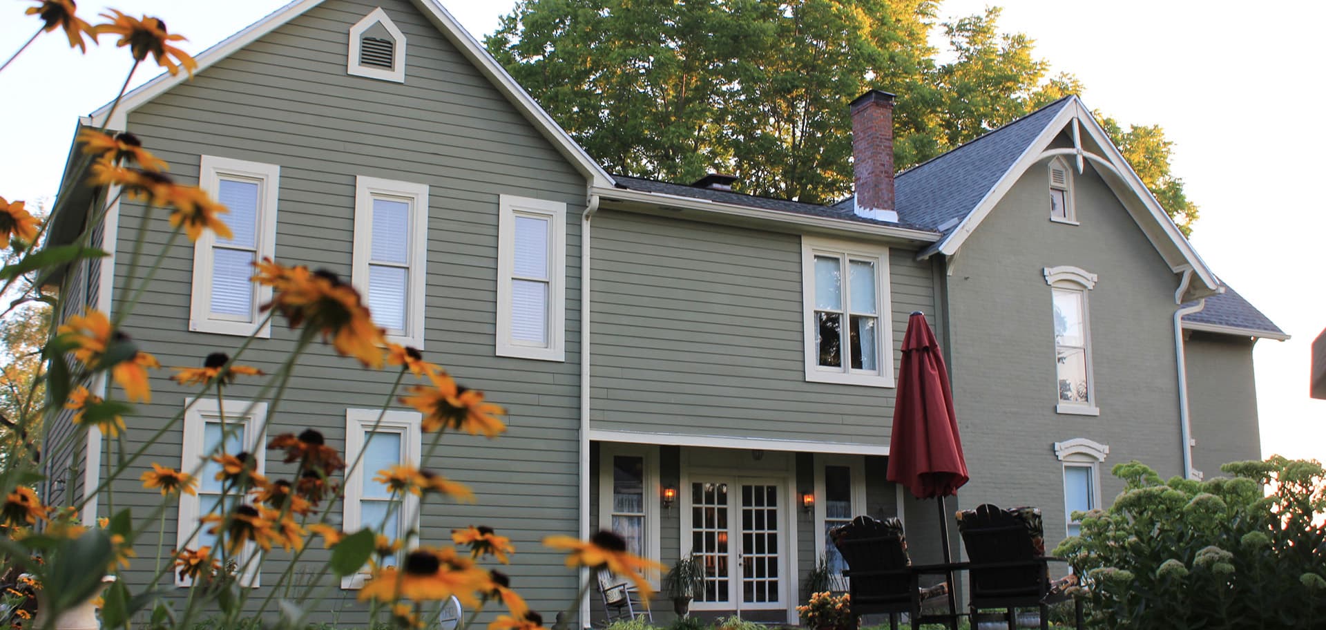 A green house with a red umbrella and flower garden in the foreground.