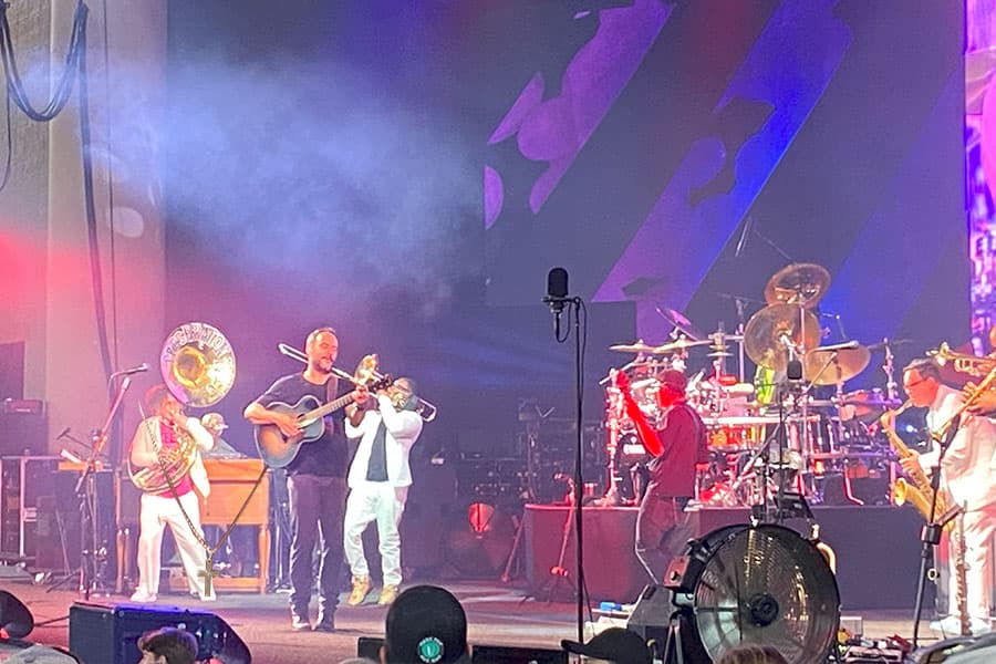 A lively band performs on stage with various instruments in front of a colorful backdrop.