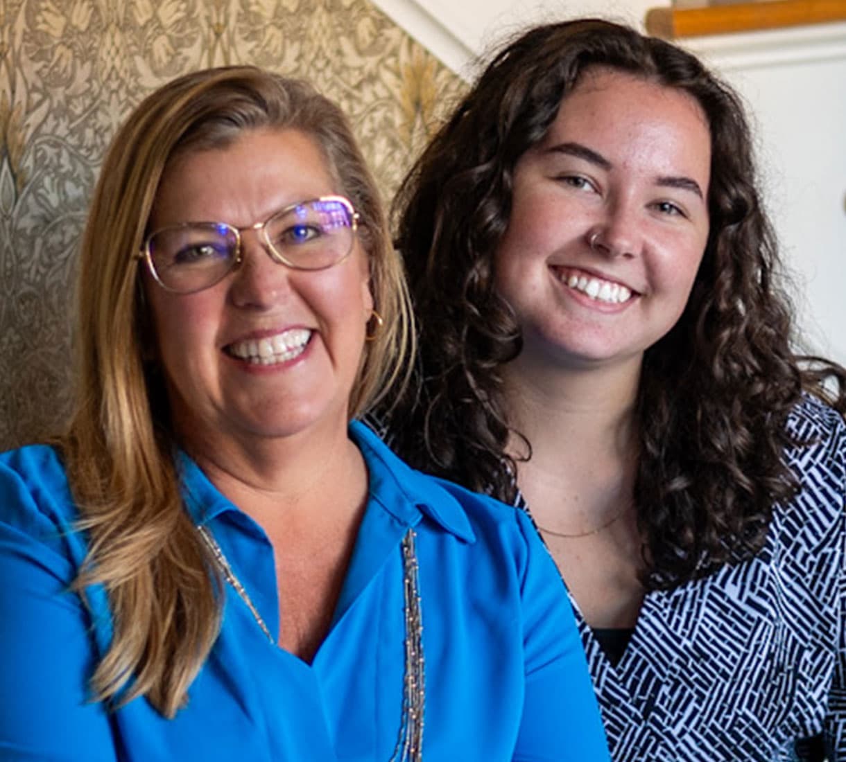 Two smiling women pose together against a patterned background.