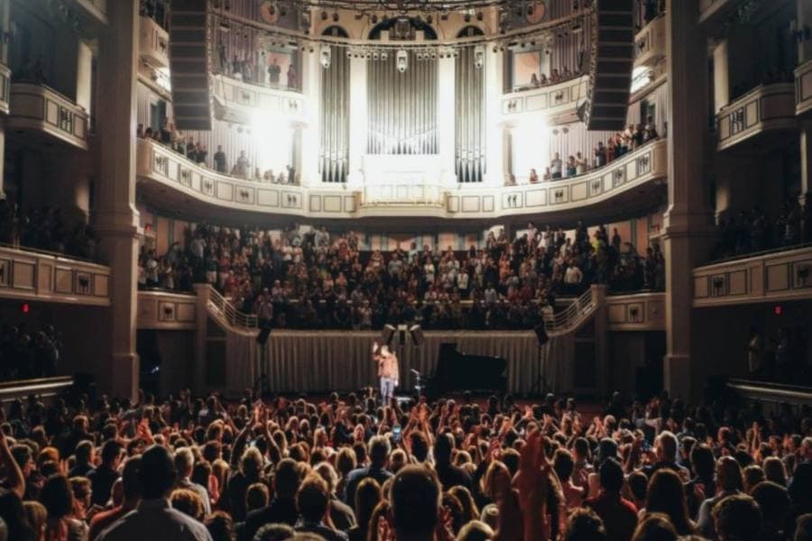 A large crowd is applauding a performer on stage in an elegant concert hall.