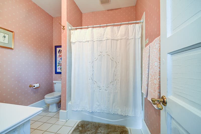 A pastel pink bathroom featuring a shower curtain, toilet, and a framed artwork on the wall.
