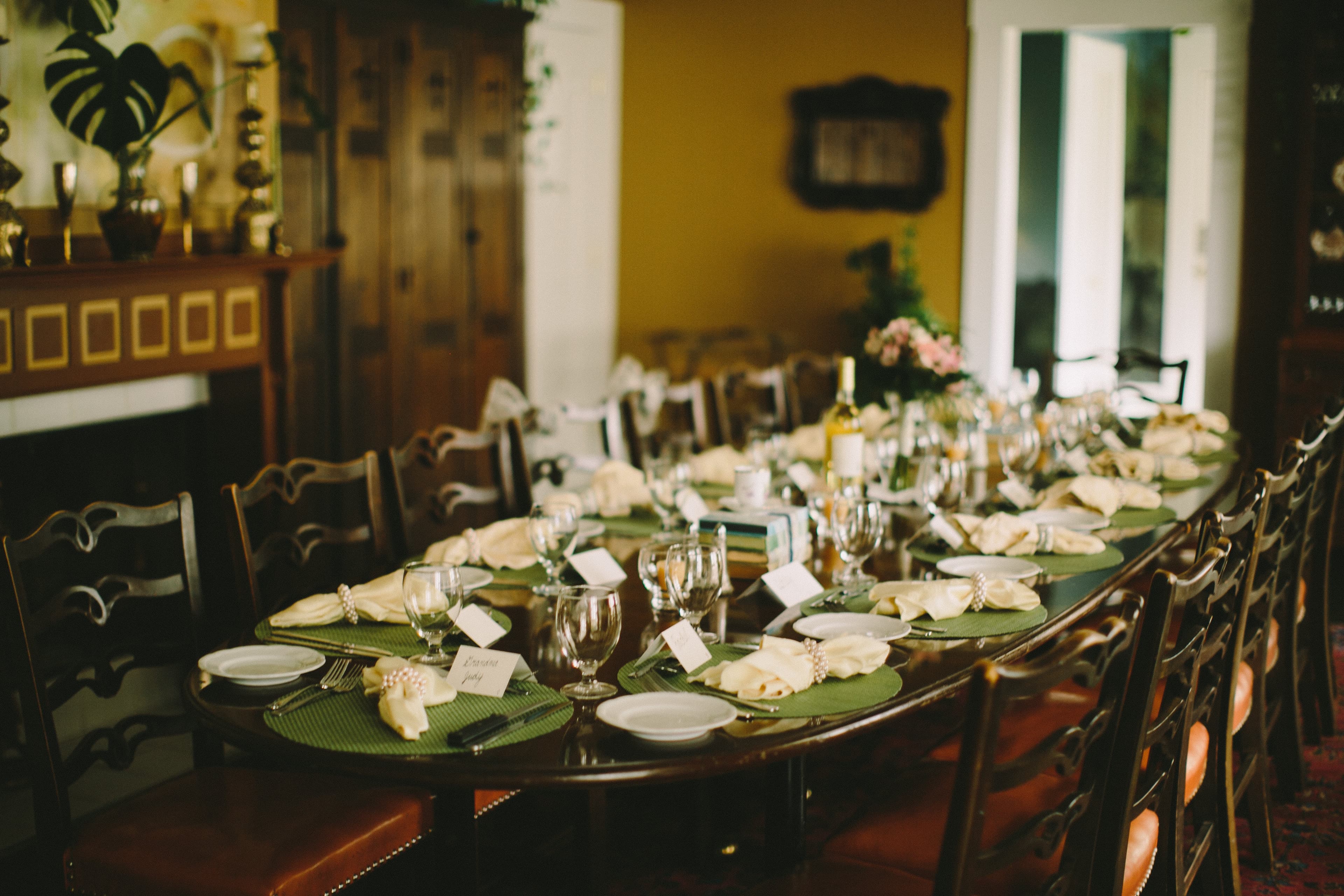 A long dining table set elegantly with glasses, plates, and folded napkins in a warmly decorated room.