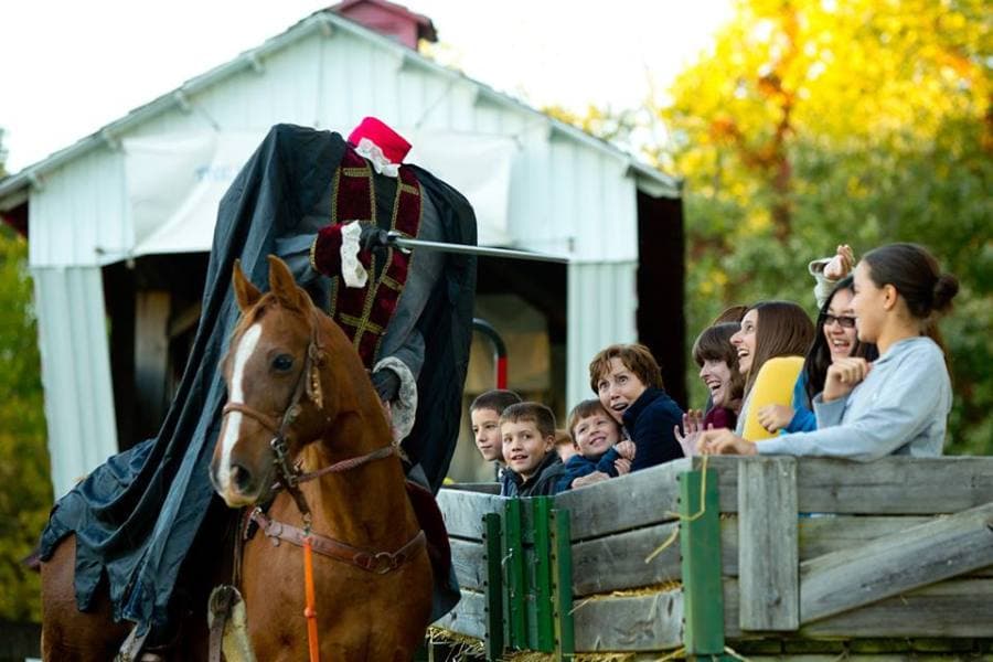 A horse carrying a headless rider in a cloak approaches a group of amused children and adults.