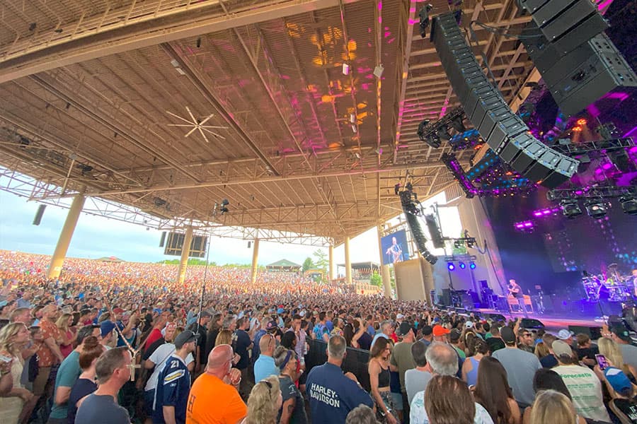 A large crowd enjoys a live concert under a covered outdoor venue.
