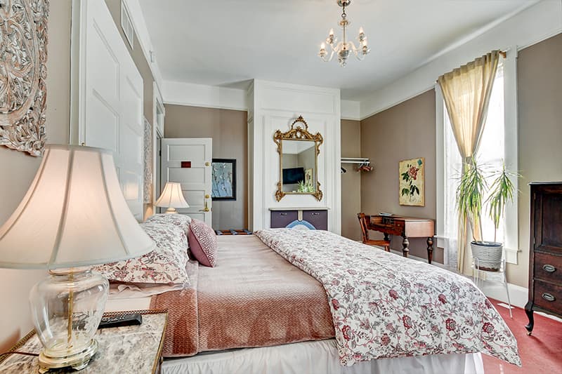 A cozy bedroom featuring a floral-patterned bedspread, elegant decor, and natural light from a nearby window.