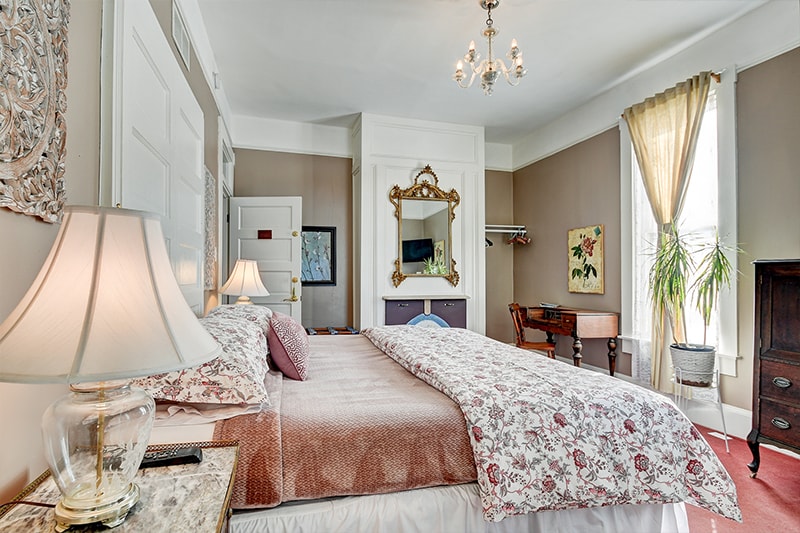 A cozy bedroom featuring a floral-patterned bedspread, elegant decor, and natural light from a nearby window.