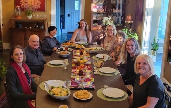 A group of eight people joyfully gathered around a beautifully set dining table with food and drinks.