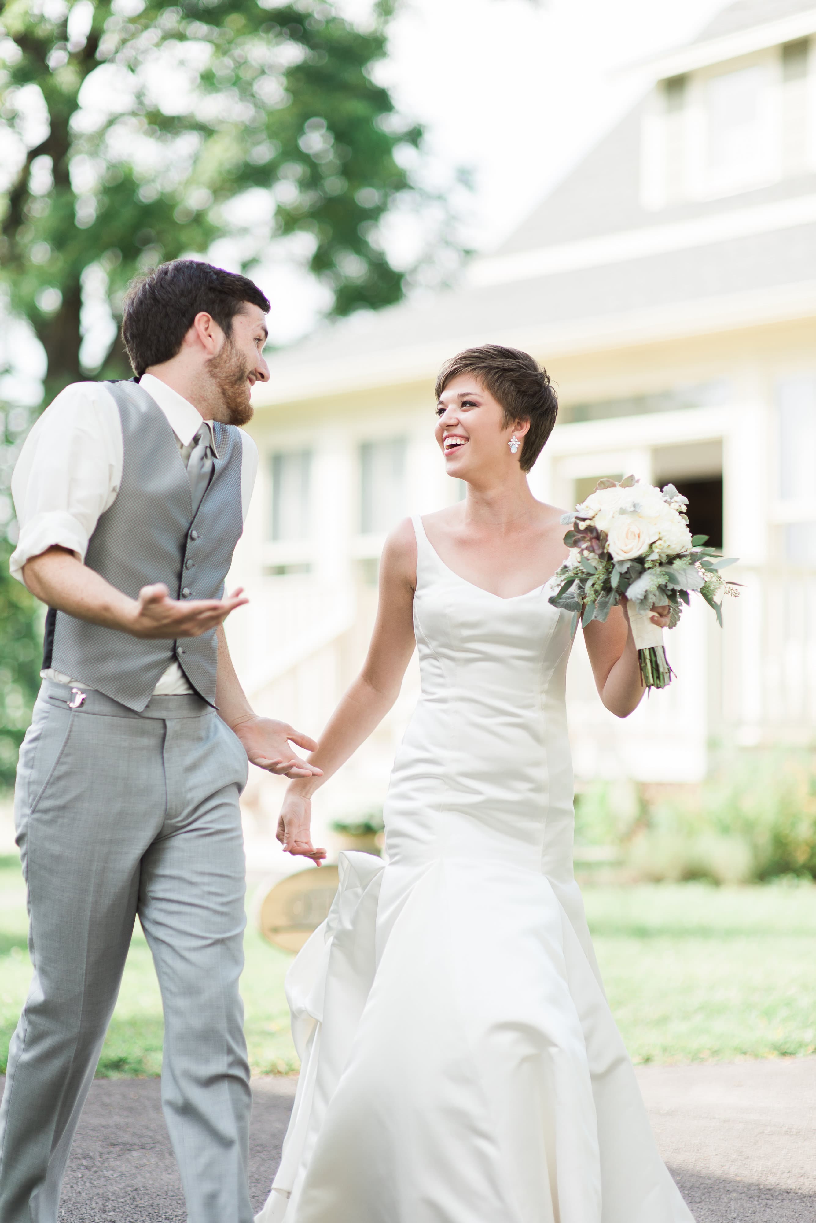 A smiling bride in a sleek wedding gown holds a bouquet while walking joyfully with the groom.