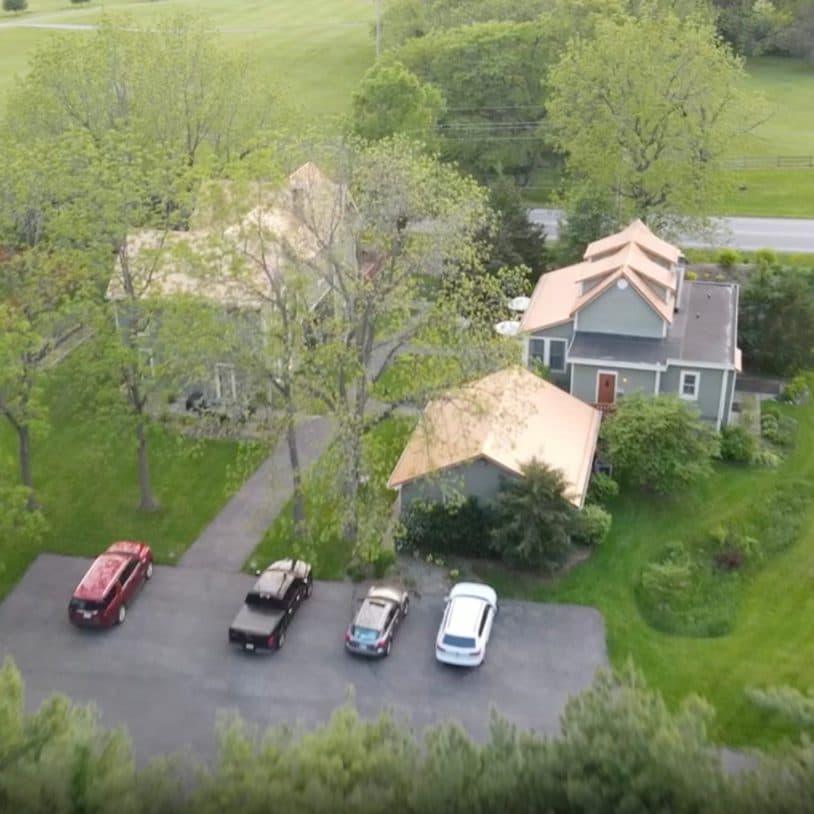 An aerial view of two houses surrounded by lush greenery, with several cars parked on a driveway.