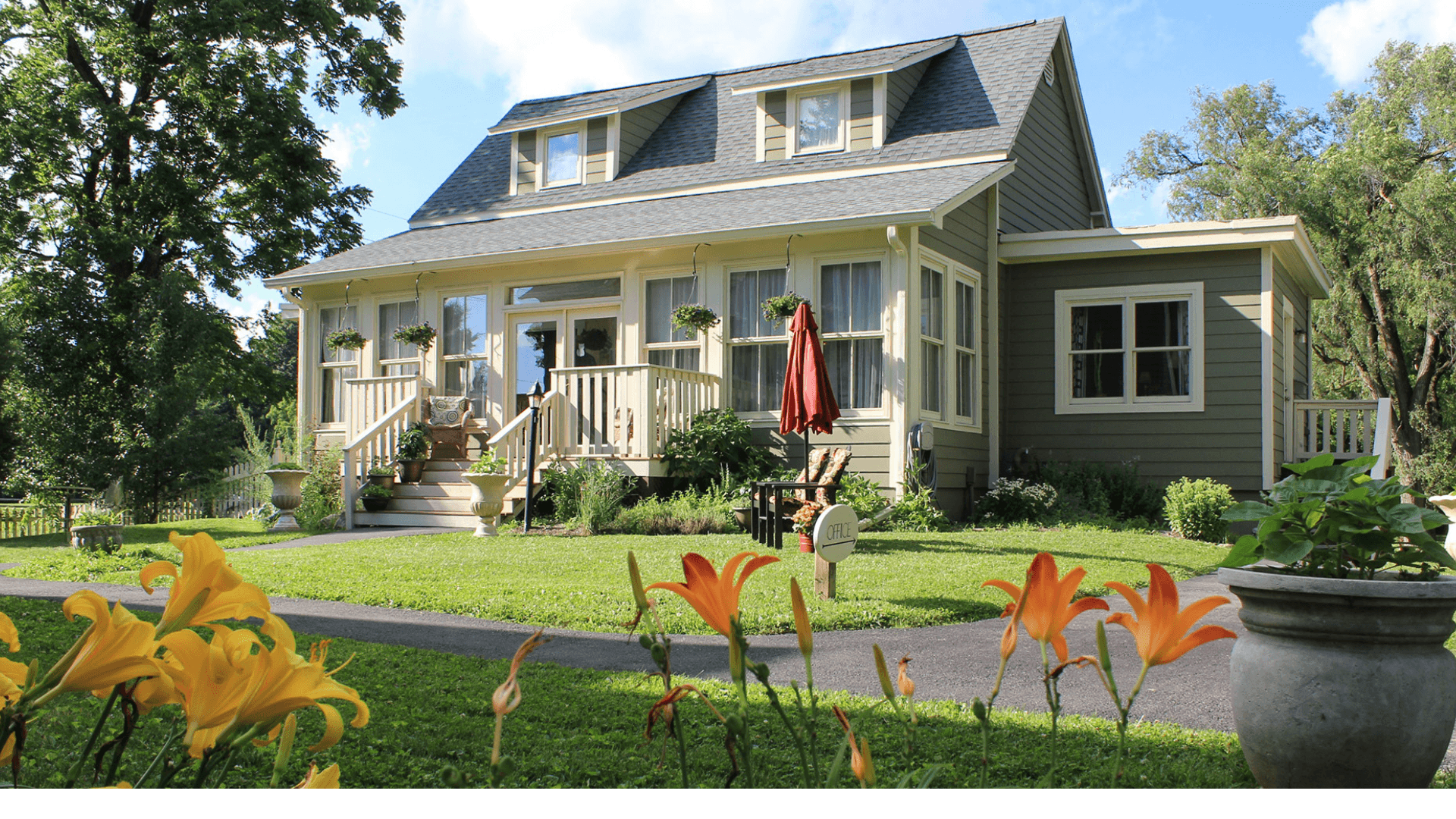 A charming green house with a porch, surrounded by flowers and trees.