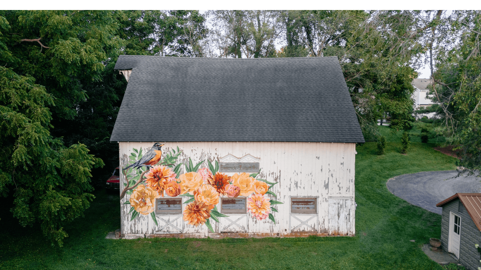 Aerial view of a barn featuring a large floral mural on one side, surrounded by greenery.
