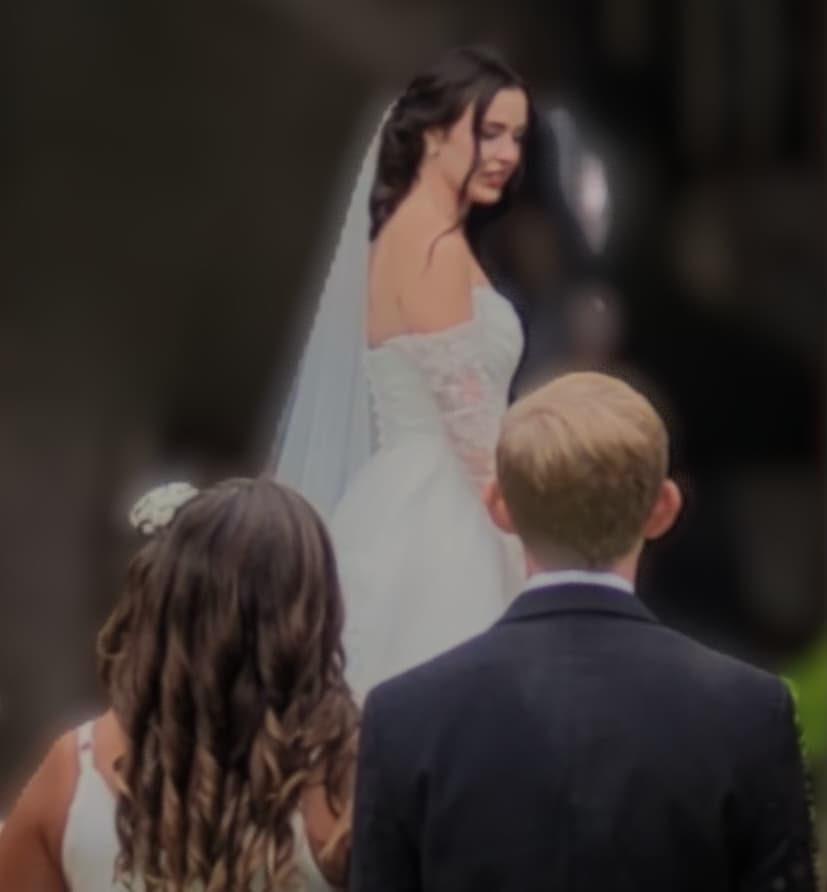 A bride in a white gown looks back at two guests from behind.
